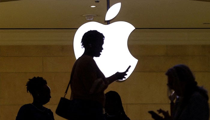 A women uses an iPhone mobile device as she passes a lighted Apple logo at the Apple store at Grand Central Terminal in New York City, US, April 14, 2023. — Reuters