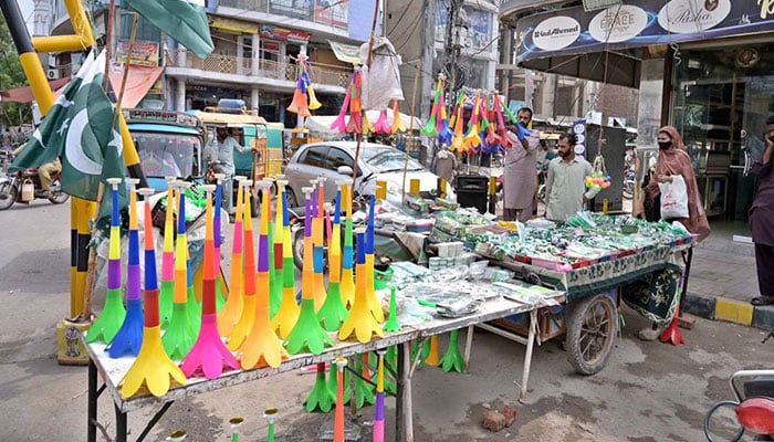 Vendor displaying national flag badges and other festive items to attract customers ahead of the upcoming Independence Day celebrations at catchahry Bzaar, Sargodha. — APP