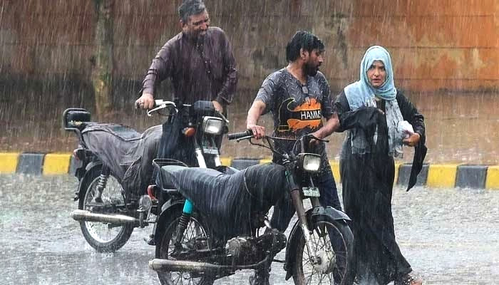 Commuters push their motorbikes along a street during a monsoon rainfall in Karachi. — AFP/File