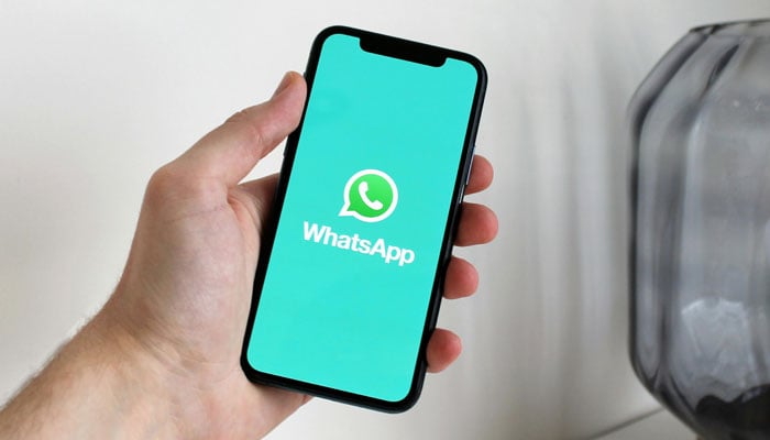 A representational image shows a person holding a phone with the WhatsApp logo displayed on its screen. — Pexels