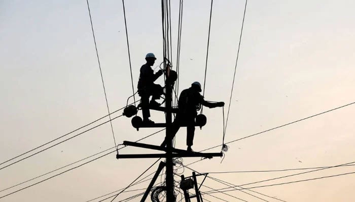 Technicians are silhouetted as they fix cables on a power transmission line in Karachi, Pakistan, January 9, 2017. — Reuters/file