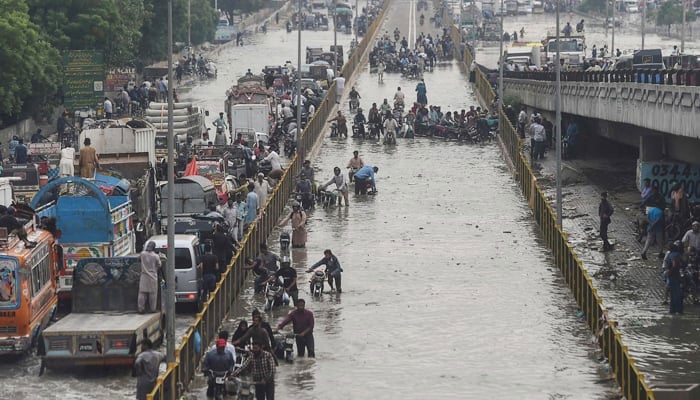 Commuters cross a flooded street after a heavy rainfall in Karachi on September 23, 2021. — AFP/file