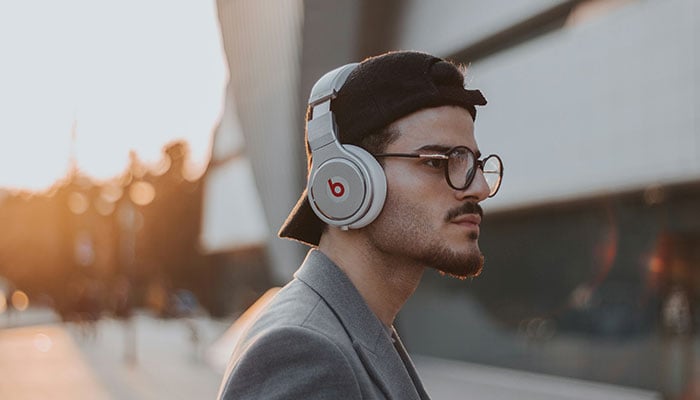 A represenatational image depicting a person wearing headphones while crossing a road in a city. — Unsplash/File