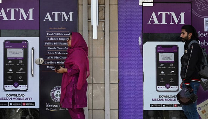 People queue along a street to use an ATM bank machine in Rawalpindi on June 9, 2023. — AFP