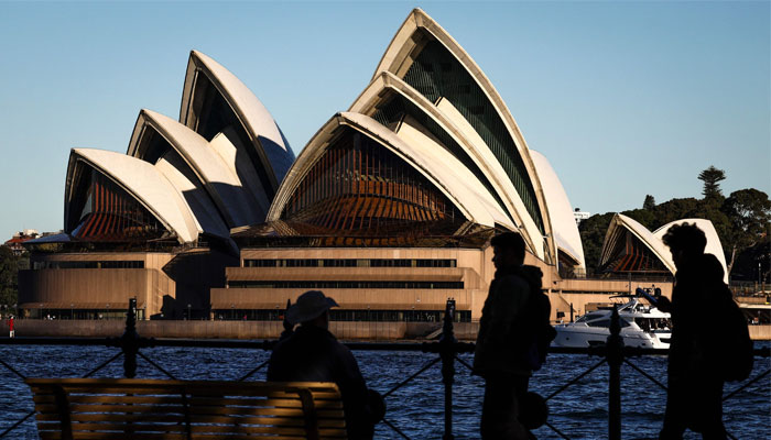 A man sits on a bench as people walk past in front of the Sydney Opera House in Sydney on June 19, 2024. — AFP