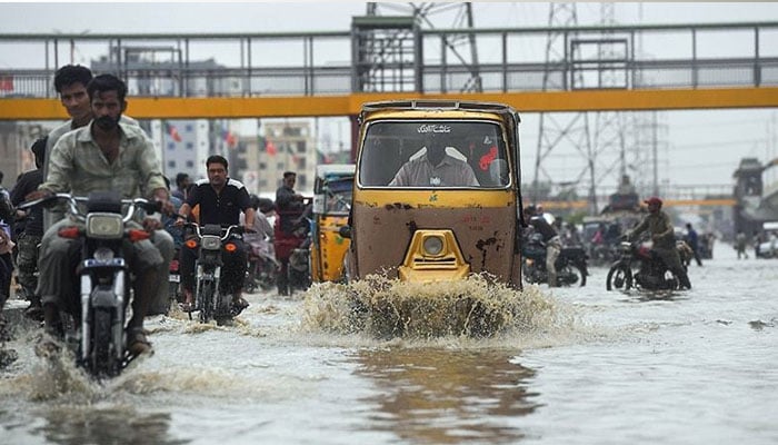 Commuters cross a flooded street during heavy monsoon rains in Karachi on July 30, 2019. — AFP