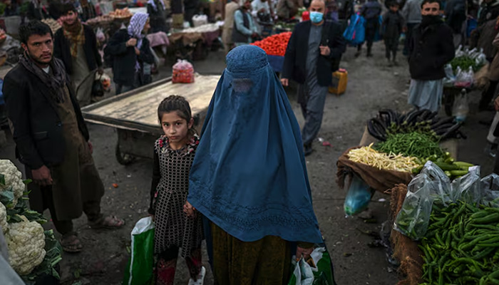 A woman wearing a burqa walks with a child in a market in Kabul. — AFP