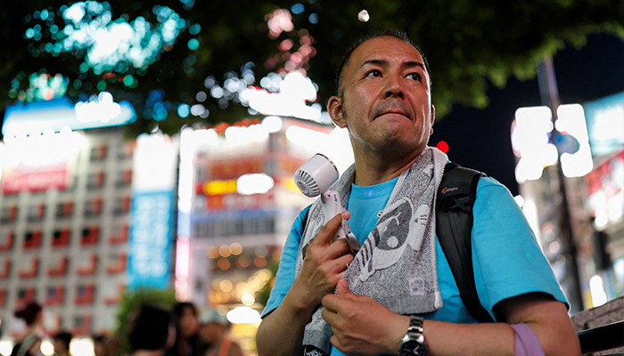 A man uses a portable fan to cool off during a hot summer day, at Tokyos Shibuya entertainment and shopping district in Tokyo, Japan on August 4, 2024.