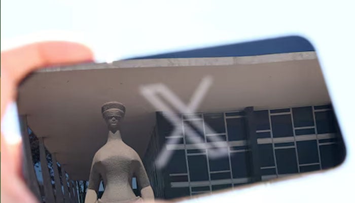 The logo of social media platform X is seen on a mobile phone next to a reflection of Brazils Supreme Court in this illustration taken August 30, 2024, in Brasilia, Brazil. — Reuters