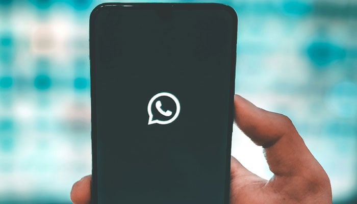 A representational image shows a person holding a phone with the WhatsApp icon displayed on its screen. — Unsplash