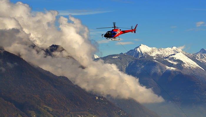 Representation image shows helicopter flying among the clouds above the snow-capped mountains. — Freepik