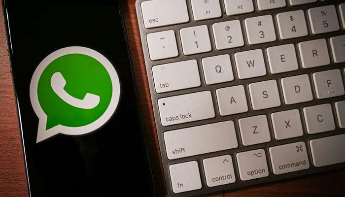 A representational image shows the WhatsApp logo displayed on a phone which is placed bnext to a keyboard. — Unsplash