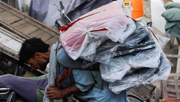 A labourer bends over as he carries packs of textile fabric on his back to deliver to a nearby shop in a market in Karachi on June 24, 2022. — Reuters