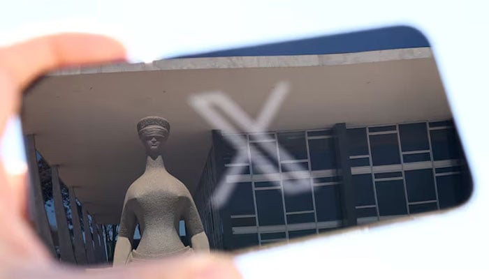 The logo of social media platform X is seen on a mobile phone next to a reflection of Brazils Supreme Court in Brasilia, Brazil on August 30, 2024. — Reuters