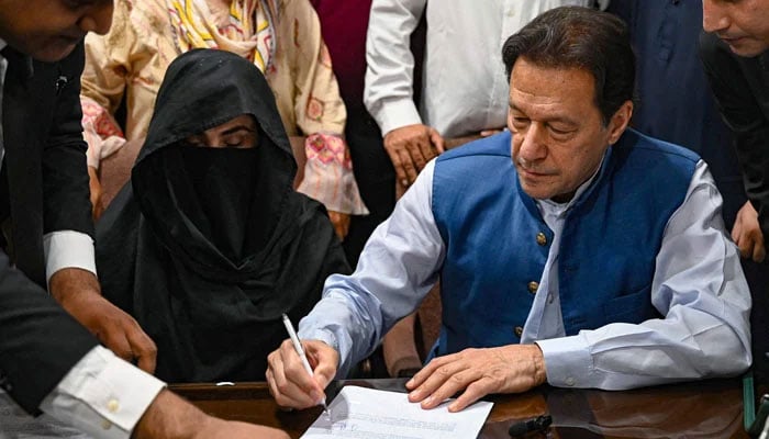 PTI founder Imran Khan (right) pictured along with his wife Bushra Bibi as he signs surety bonds for bail in various cases, at a registrars office in the Lahore High Court, in Lahore on July 17, 2023. — AFP