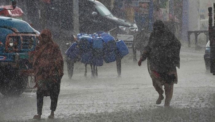 A representational image showing people walking amid heavy rainfall. — AFP/File