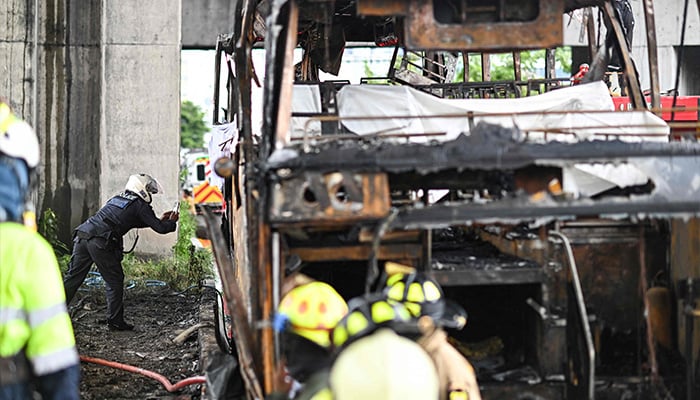 A police officer takes photographs as he inspects the back of a burnt-out bus that was carrying students and teachers on the outskirts of Bangkok, Thailand, on October 1, 2024. — AFP