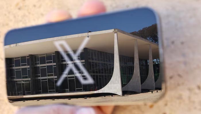 The logo of social media platform X is seen on a mobile phone next to a reflection of Brazils Supreme Court in this illustration taken August 30, 2024, in Brasilia, Brazil. — Reuters