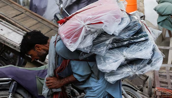 A labourer bends over as he carries packs of textile fabric on his back to deliver to a nearby shop in a market in Karachi on June 24, 2022. — Reuters