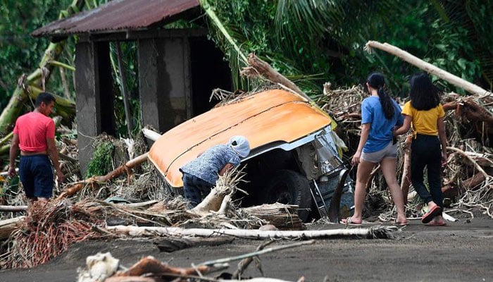 Residents examine a buried passenger jeepney swept away retrieve by floods during heavy rains brought about by Tropical Storm Trami in Laurel town, Batangas province, south of Manila on October 25, 2024. — AFP