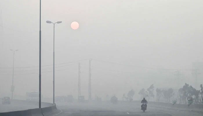 A man rides a motorbike along a street engulfed in dense smog, in Lahore on October 23, 2024. — AFP