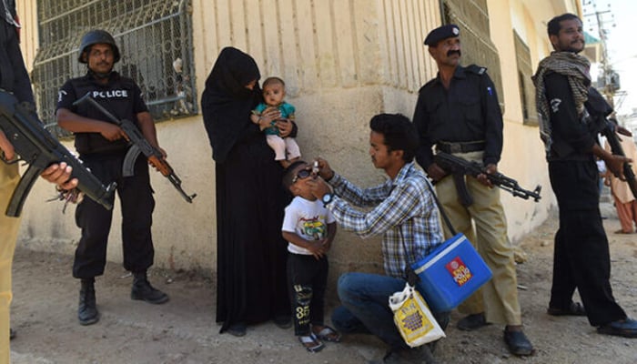 A volunteer administers the polio vaccine to a child amid police security in this undated photo. — APPLICATION/File