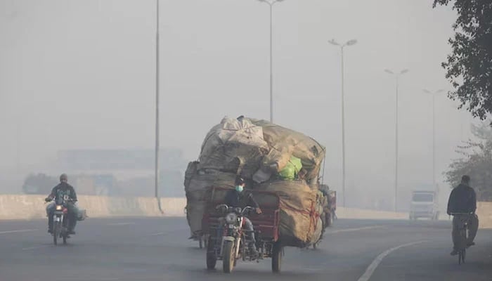 A man rides a motor tricycle, loaded with sacks of recyclables, amid dense smog in Lahore on November 24, 2021. — Reuters