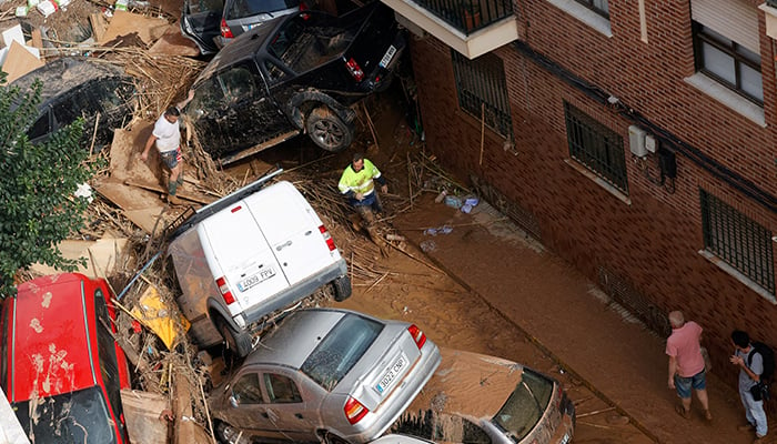 People walk alongside cars piled up on a street in the aftermath of torrential rains that caused flooding, in Paiporta, Spain, October 31, 2024. — Reuters