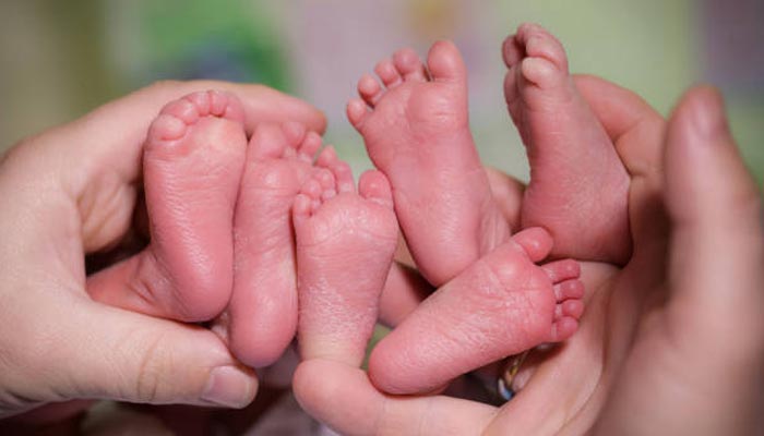 A representational image showing a person holding up the feet of three babies. — Pexels