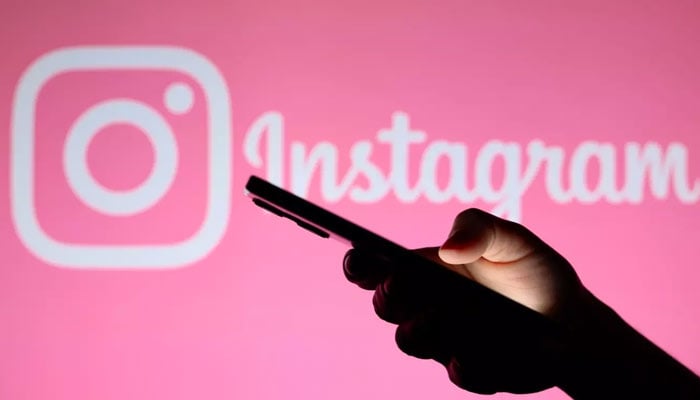 A person uses a phone in front of a pink screen displaying Instagram logo. — Reuters