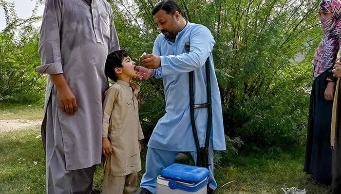 A health worker (C) administering polio drops to a child during a door-to-door poliovirus vaccination campaign on the outskirts of Peshawar. — AFP