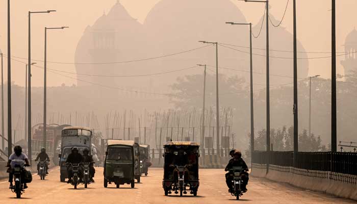 Commuters ride along a street engulfed in smog, in Lahore on November 5, 2024. — AFP