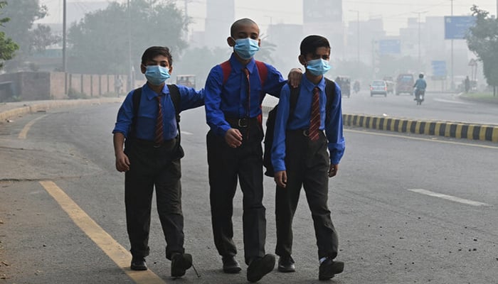 School boys wear masks as they walk along a road amid heavy smog in Lahore on October 29, 2024. — AFP