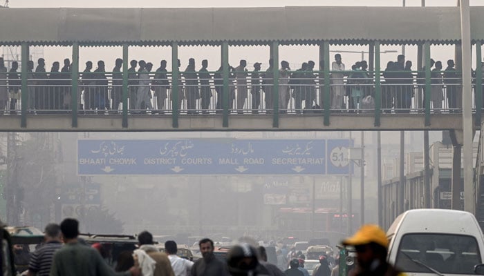 People align on a pedestrian bridge across a street engulfed in smog, in Lahore on November 5, 2024. — AFP