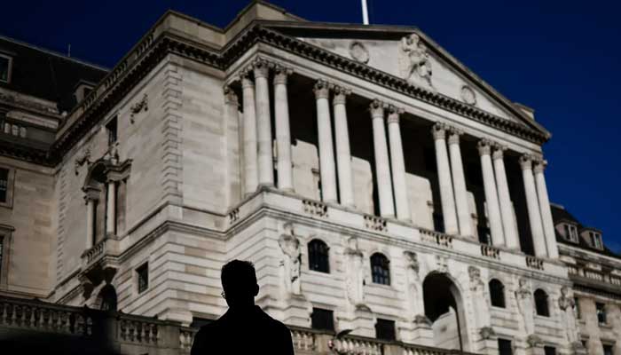 A pedestrian crosses the streets in front of The Bank of England illuminated by a ray of sunlight, in central London, on February 12, 2024. — AFP