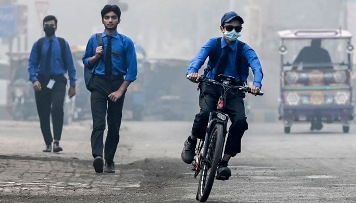 A student wearing a mask rides a bicycle to school along a street engulfed in smog, in Lahore on November 5, 2024. — AFP