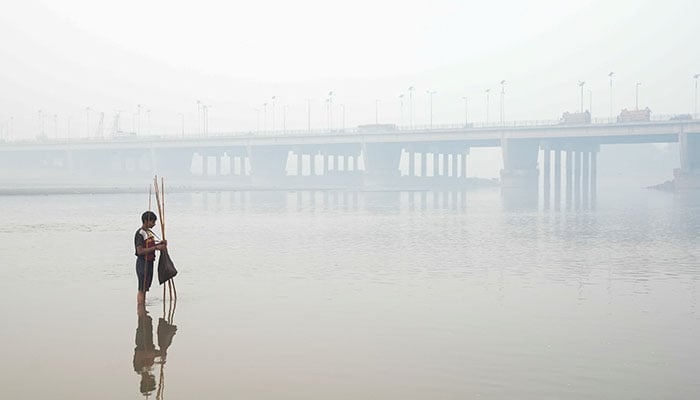 A person sets up a fishing trap, with the bridge over the River Ravi in the background, amid smog in Lahore on November 5, 2024. — Reuters