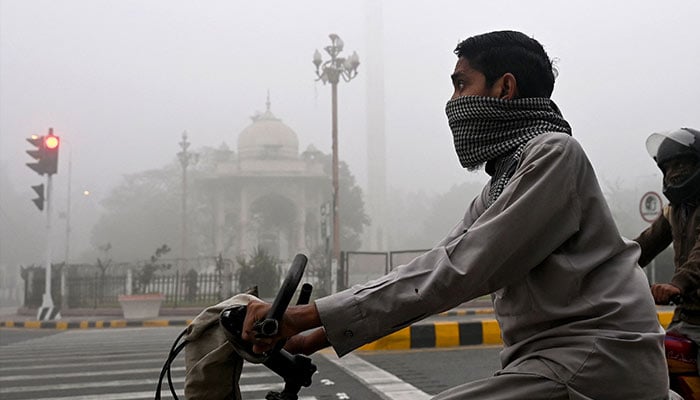 Commuters ride along a street engulfed in smog in Lahore on November 14, 2024. — AFP