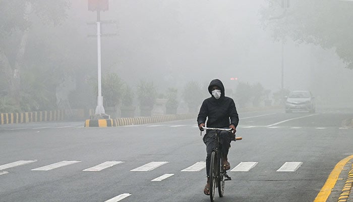 A man rides his bicycle along a street engulfed in smog in Lahore on November 14, 2024. — AFP