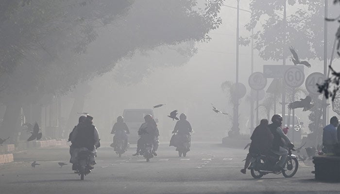 Commuters ride along a street engulfed in smog in Lahore on November 18, 2024.