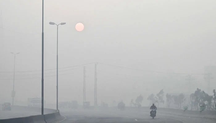 A man rides a motorbike along a street engulfed in dense smog, in Lahore on October 23, 2024. — AFP