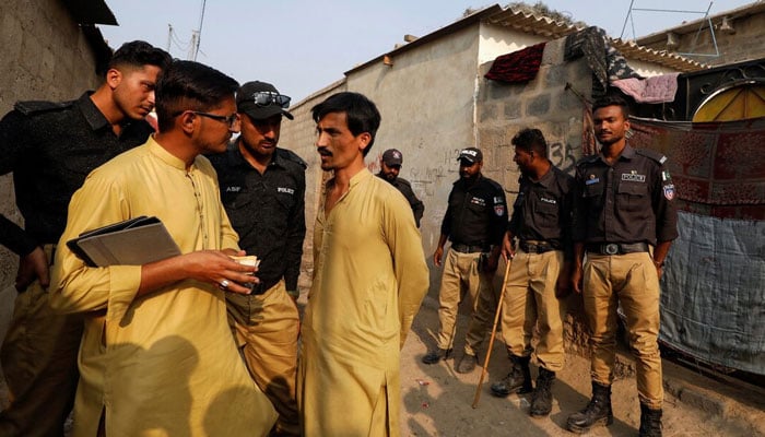 A Nadra worker, along with police officers, speaks to a resident while checking identity cards, during a door to door search and verification drive for undocumented Afghan nationals, in an Afghan Camp on the outskirts of Karachi, November 21, 2023. — Reuters