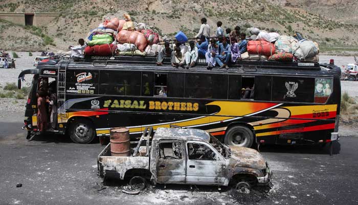 A bus with passengers sitting on the roof with belongings, drives past a damaged vehicle, a day after militants conducted deadly attacks, in Bolan district of Balochistan, August 27, 2024. — Reuters