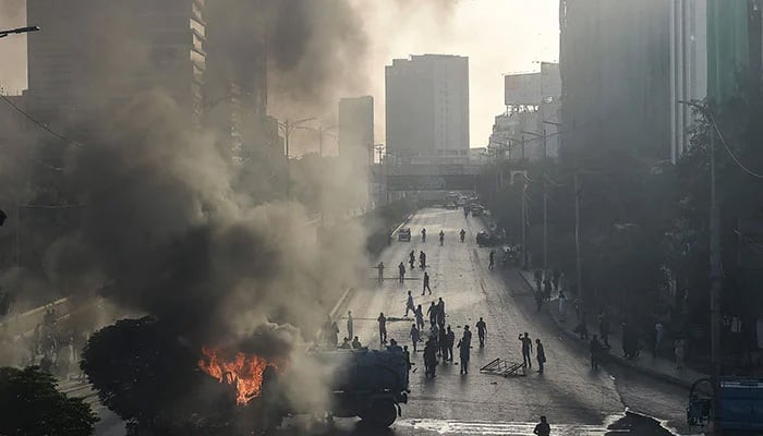 PTI activists and supporters of former prime minister Imran Khan gather beside burning water tanker on a blocked road during a protest against the arrest of their leader in Karachi on May 9, 2023. — AFP