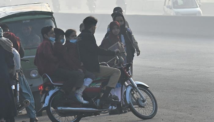 A man rides a motorcycle carrying school children amid heavy smog in Lahore on November 25, 2024. — AFP