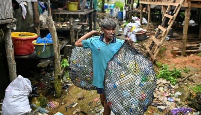 A Moken fisherman carries bags of plastic waste to sell to Tide staff members at his fishing village on Thailands southern island of Koh Chang. — AFP/File