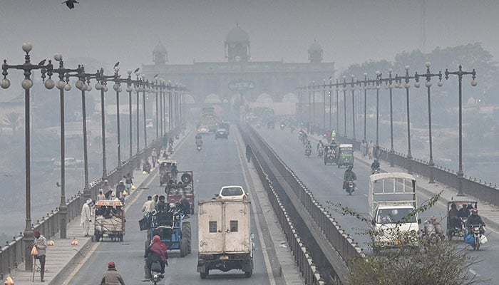 Commuters move along a road amid smoggy conditions in Lahore on November 24, 2024. — AFP