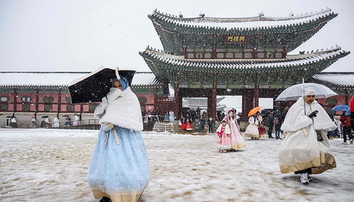 Visitors wearing traditional hanbok dresses are seen on the grounds of Gyeongbokgung Palace amid heavy snowfall in Seoul on November 27, 2024. — AFP