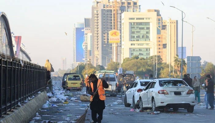 A worker clears the road, with damaged vehicles in the background, after security forces launched a raid on supporters of Pakistan Tehreek-e-Insaf who had stormed the capital demanding Imran Khans release on  November 27, 2024. — Reuters