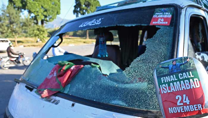 Commuters ride past a vehicle that was damaged by PTI supporters in Islamabad on November 27, 2024. — AFP